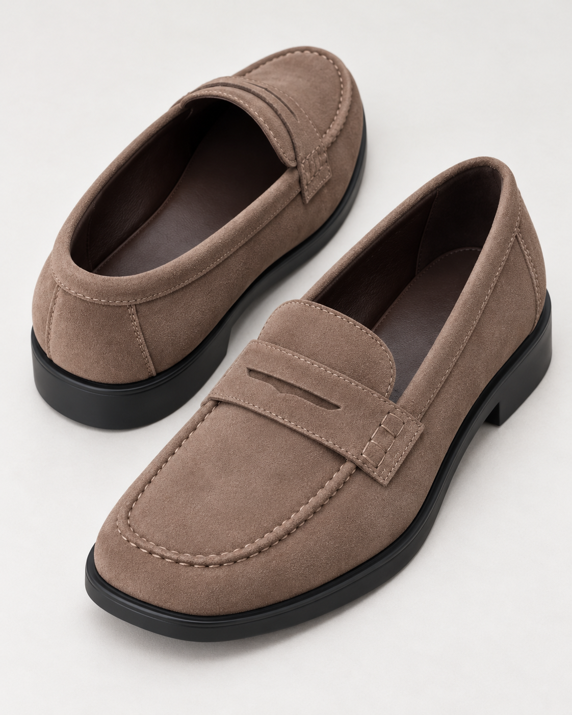 Tan suede penny loafer, shown from the side with moc-toe stitching and a black low block heel.